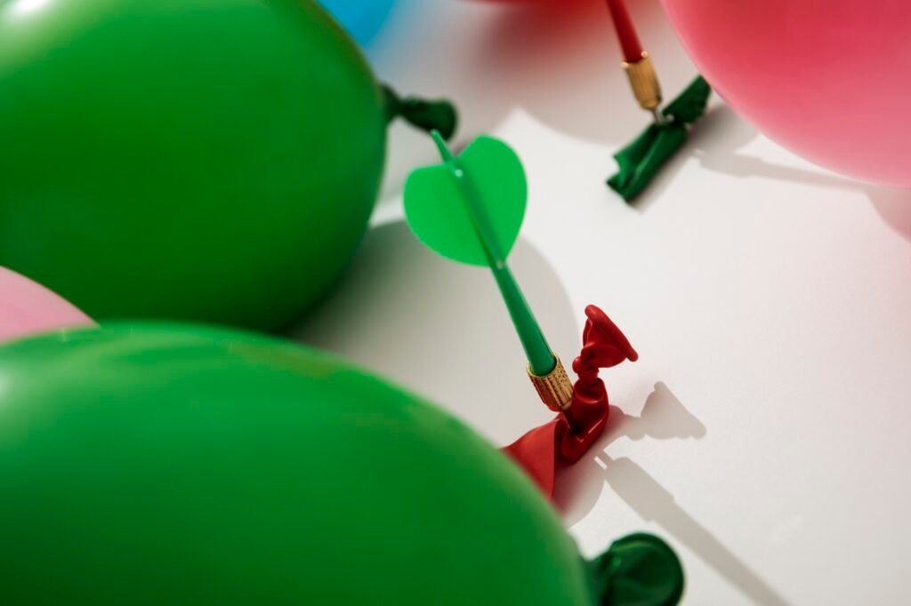green dart piercing a deflated red balloon surrounded by green and pink balloons, symbolizing focus, precision, and overcoming challenges with Tadah!'s coaching strategies for professional growth and resilience